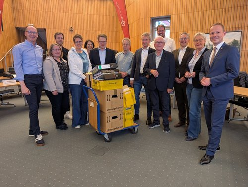 Die Mitgliederinnen und Mitglieder des Kreiswahlausschusses stehen in der Mitte des Großen Sitzungssaals. Im Vordergrund ein Handwagen mit den Wahlunterlagen. 