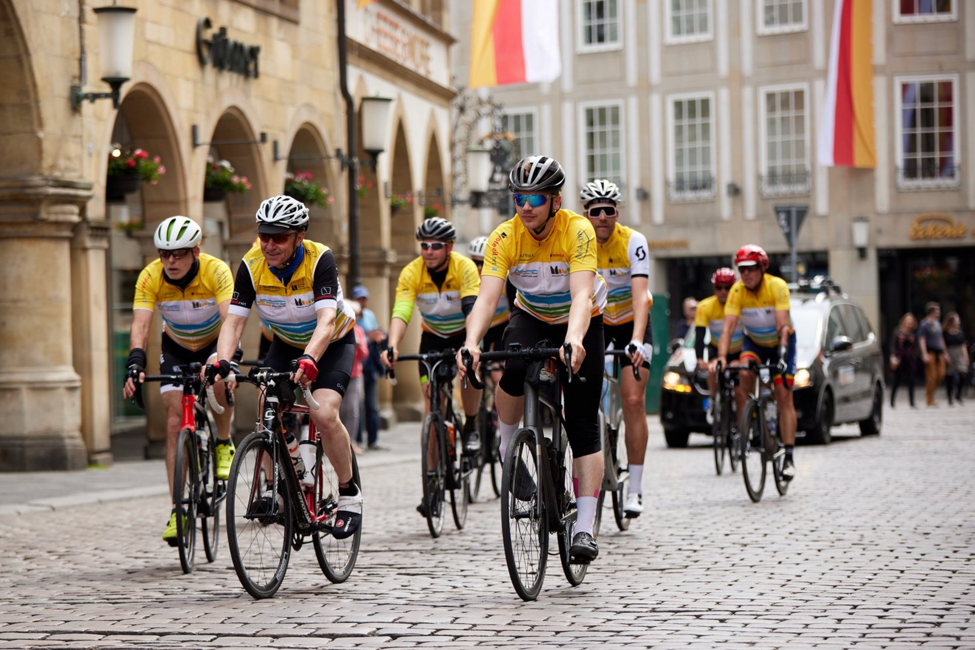 Eine Gruppe von Radfahrern in gelben trikots fährt über einen Platz mit Kopfsteinpflaster.