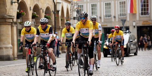 Eine Gruppe von Radfahrern in gelben trikots fährt über einen Platz mit Kopfsteinpflaster.