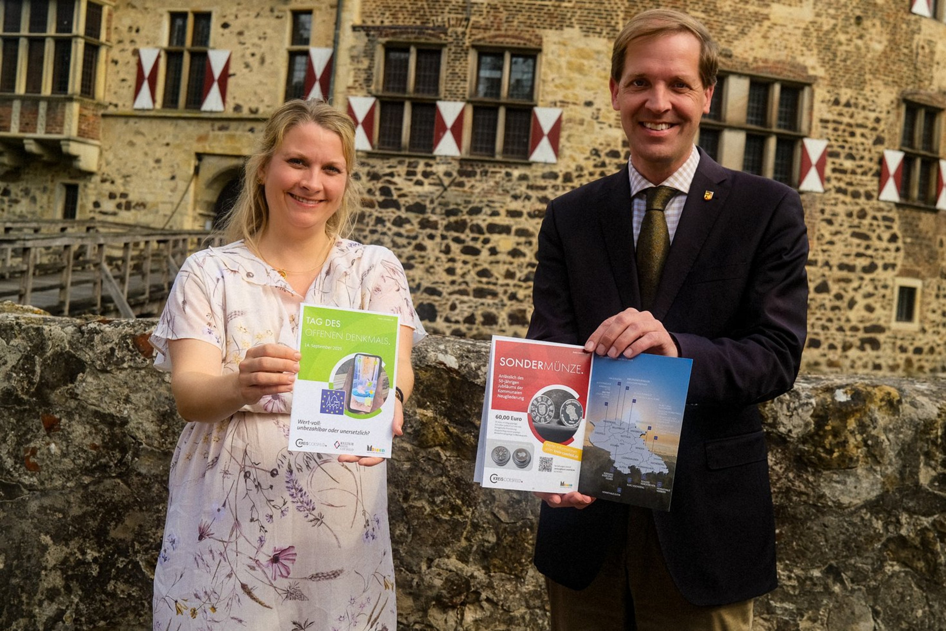 Kulturreferentin Swenja Janning und Landrat Dr. Christian Schulze Pellengahr präsentieren die Broschüre zum Tag des offenen Denkmals (Foto: Kreis Coesfeld, Lukas Bertels). Eine Frau und ein Mann stehen vor einem Bachsteingebäude und halten zwei Broschüren in die Kamera.