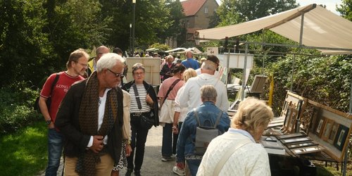 Menschen laufen auf einer Straße, an der ein Stand aufgebaut ist, auf dem gerahmte Bilder liegen.