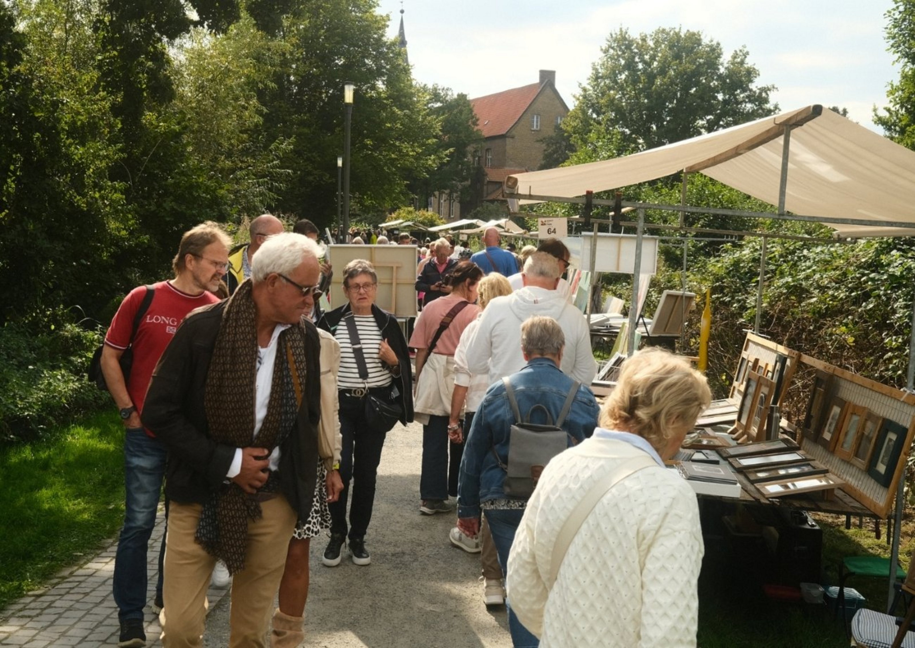 Menschen laufen auf einer Straße, an der ein Stand aufgebaut ist, auf dem gerahmte Bilder liegen.