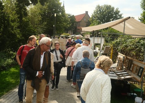 Menschen laufen auf einer Straße, an der ein Stand aufgebaut ist, auf dem gerahmte Bilder liegen.