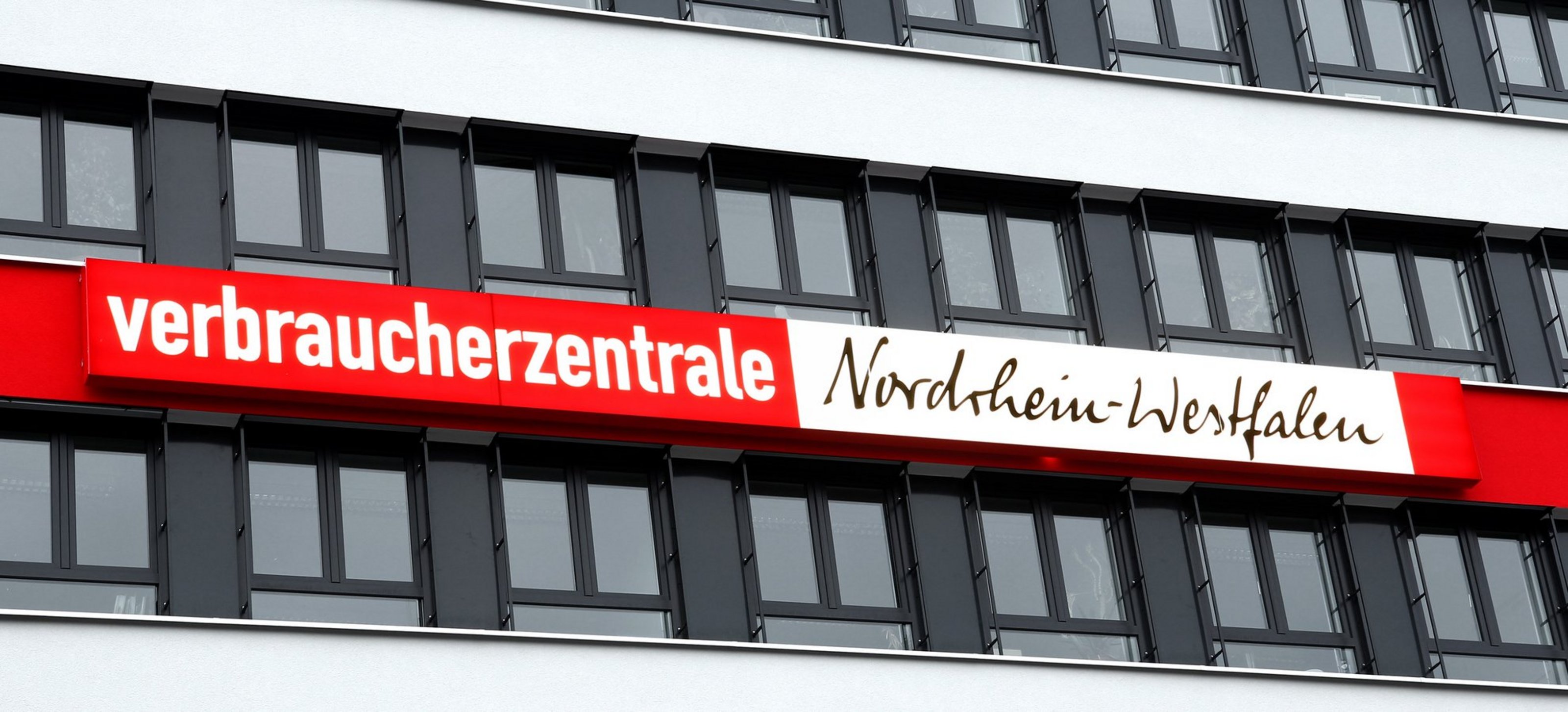 Eine Gebäudefassade mit vielen Fenstern und dem Schriftzug "Verbraucherzentrale Nordrhein-Westfalen" ist zu sehen.