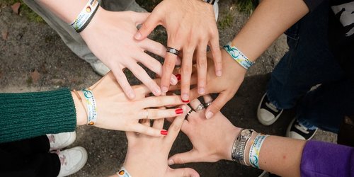 Fünf Hände sind in die Mitte des Bildes gestreckt und von oben fotografiert.