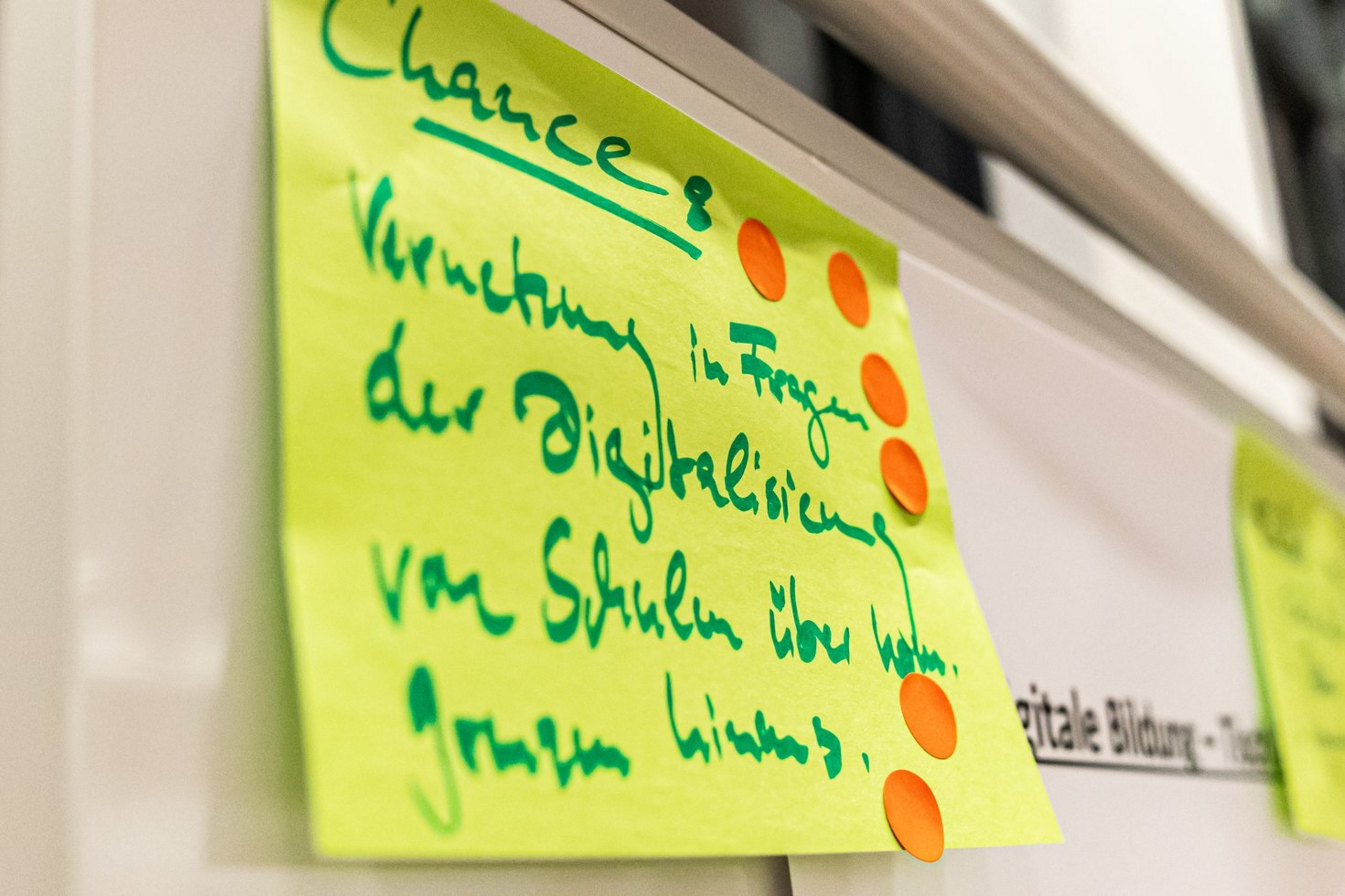 Nahaufnahme von gelben Haftnotizen mit handschriftlichen grünen Texten und farbigen Punkten an einer weißen Wand