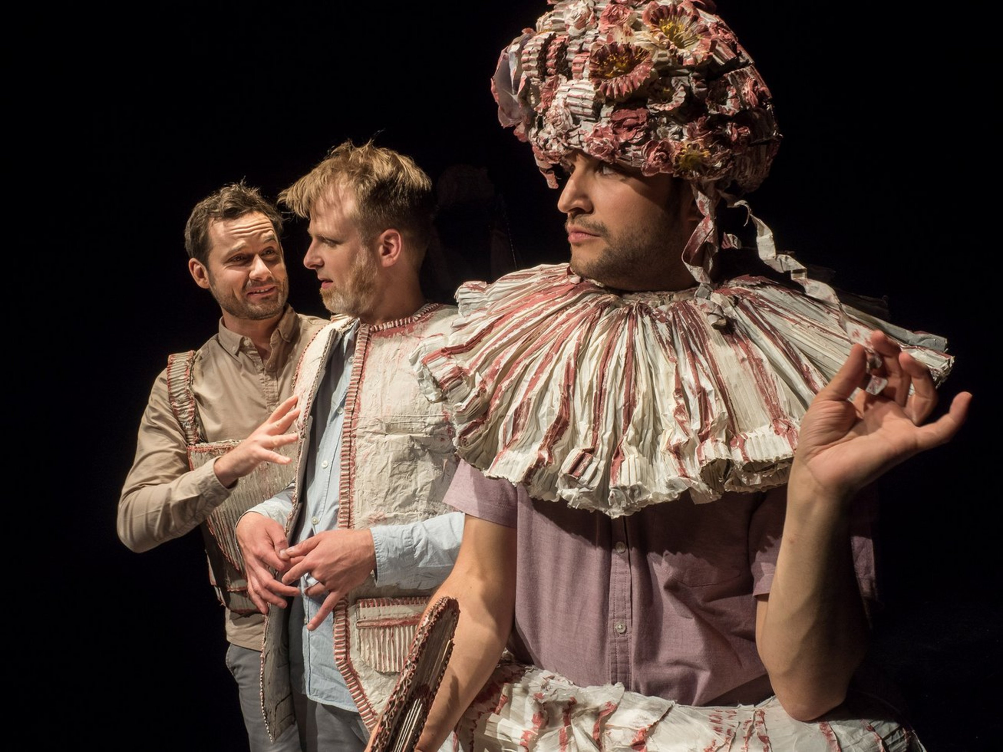 Mit der „Jungen Bühne Münsterland“ tourt ein Kulturprogramm speziell für junge Menschen durch die Region. Das echtzeit-theater gastiert dabei mit dem Stück „Das besondere Leben der Hilletje Jans“ (Foto: Roman Starke). Drei Männer in Kostümen vor schwarzem Hintergrund. Die Kostüme sind teilweise aus Papier. Der Mann rechts trägt einen Hut mit Papierblumen.