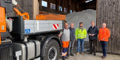 Neben einem Laster stehen vier Männer. Sie befinden sich vor einer halle, in der ein Berg Salz aufgeschüttet ist.