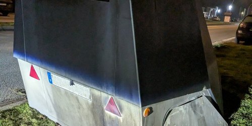 Ein Geschwindigkeitsmessgerät steht am Straßenrand. Das Gehäuse ist an der rechten Seite geöffnet.