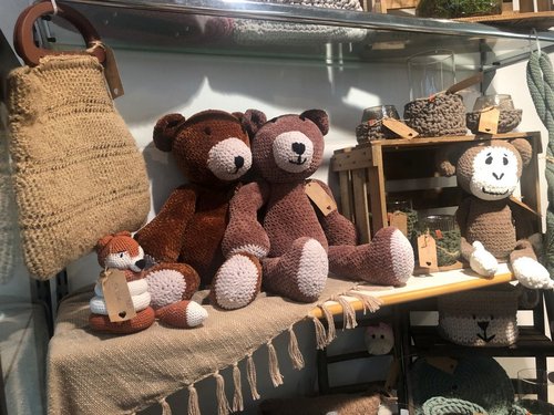 Gehäkelte Stofftiere und handgefertigte Dekorationsartikel aus Wolle und Garn auf einem Verkaufsregal eines Kunsthandwerksstands.