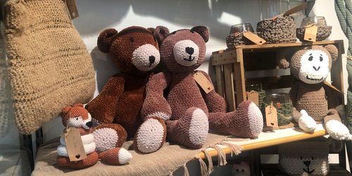 Gehäkelte Stofftiere und handgefertigte Dekorationsartikel aus Wolle und Garn auf einem Verkaufsregal eines Kunsthandwerksstands.