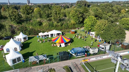 Blick von oben auf das Baumberge Culture Camp mit buntem Zirkuszelt, weißen Pavillons und vielen Besuchern auf einer Wiese.