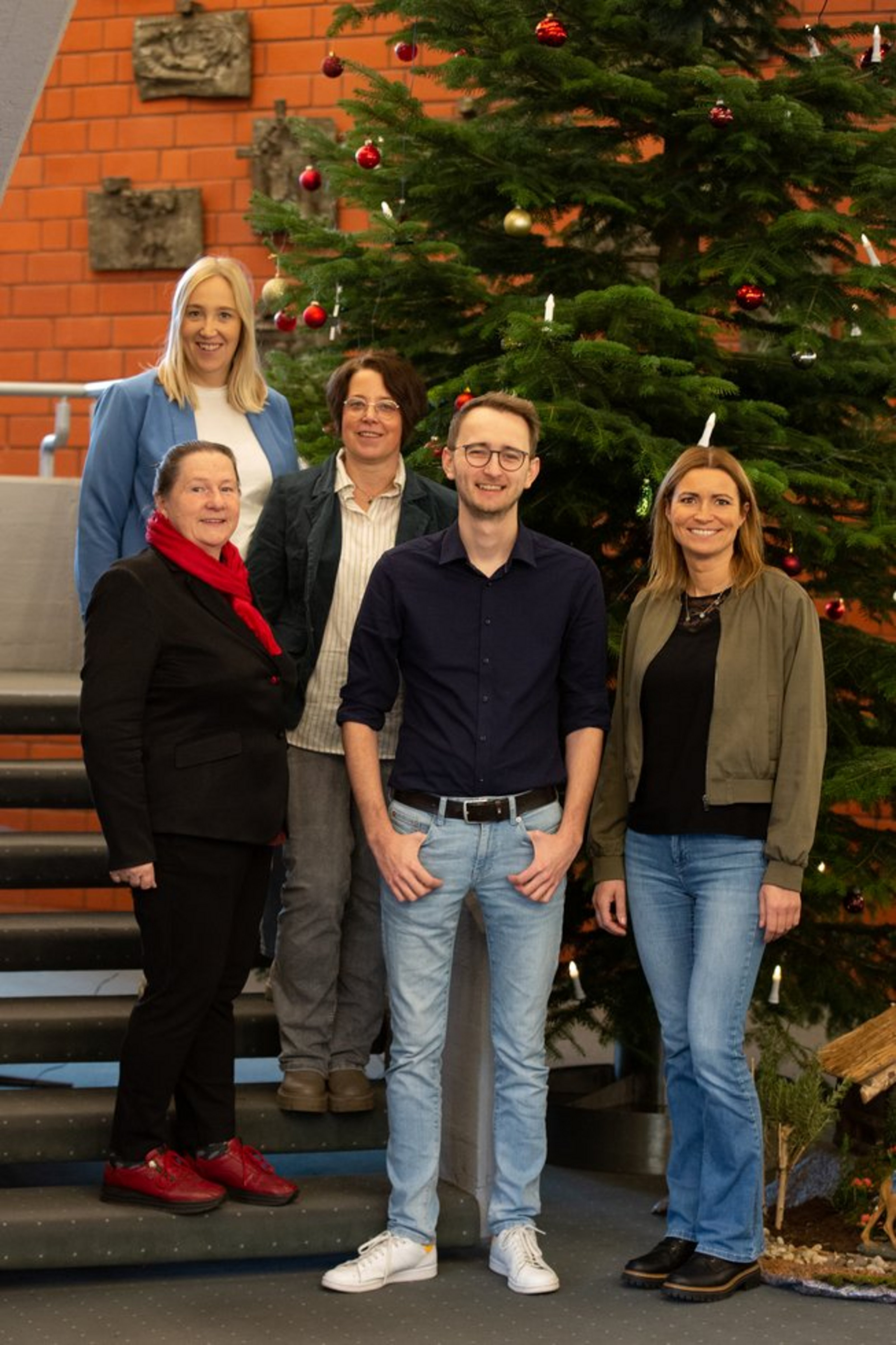 Fünf Personen stehen auf einer Treppe neben einem Weihnachtsbaum.