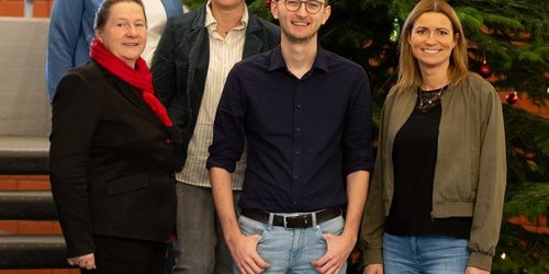 Fünf Personen stehen auf einer Treppe neben einem Weihnachtsbaum.