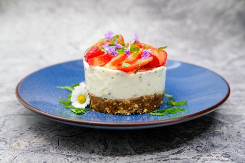 Auf einem blauen Teller ist ein Gericht mit Erdbeeren, Gänseblümchen, lila Blüten und einer weißen Creme angerichtet.
