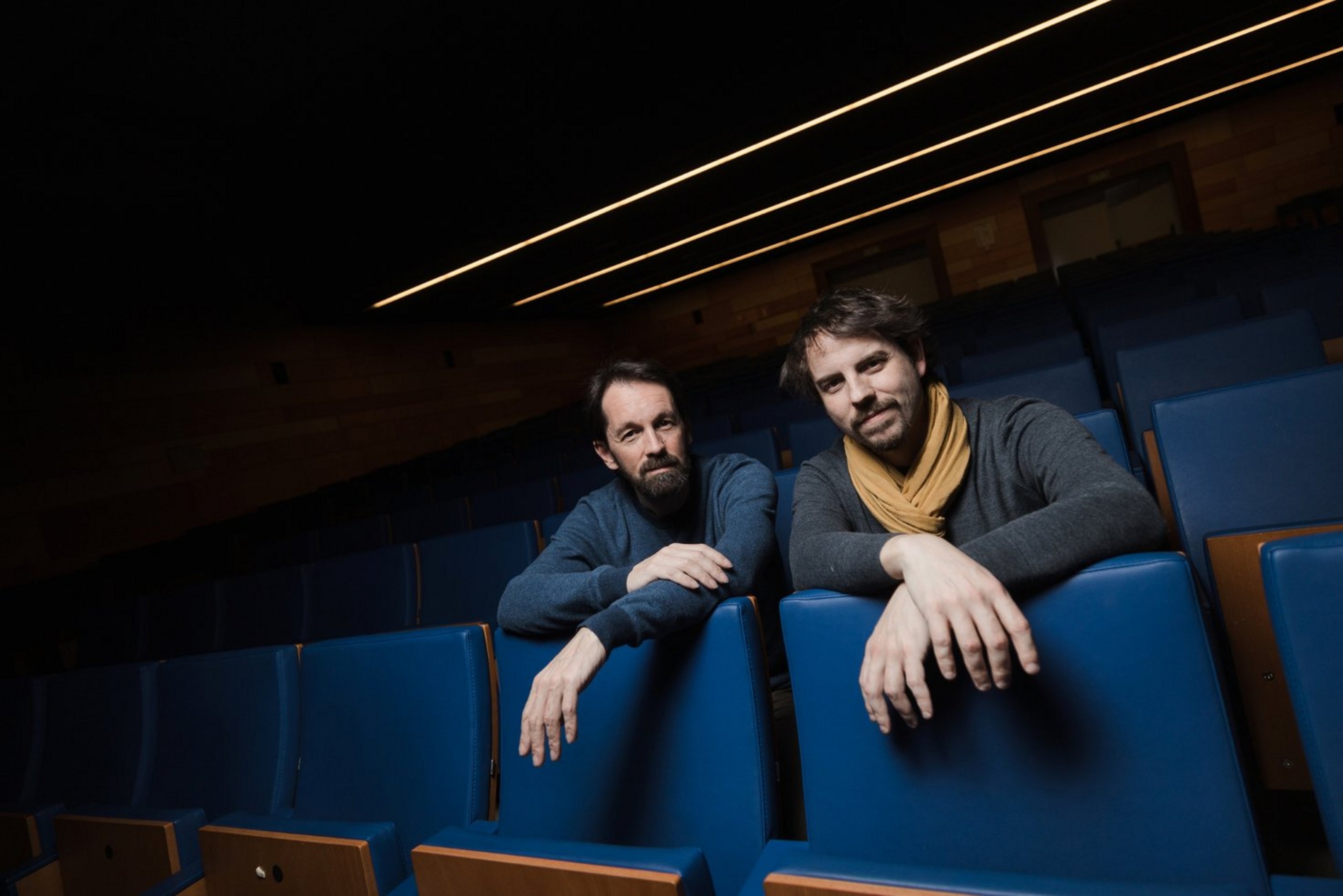 Daniel García (Piano) und Pablo Martín Caminero (Kontrabass) (Foto: Rodrigo Mena) Zwei Männer sitzen in einem Saal mit blauen Klappsesseln, ihre Arme liegen verschränkt auf den Lehnen der Sitzreihen vor ihnen.