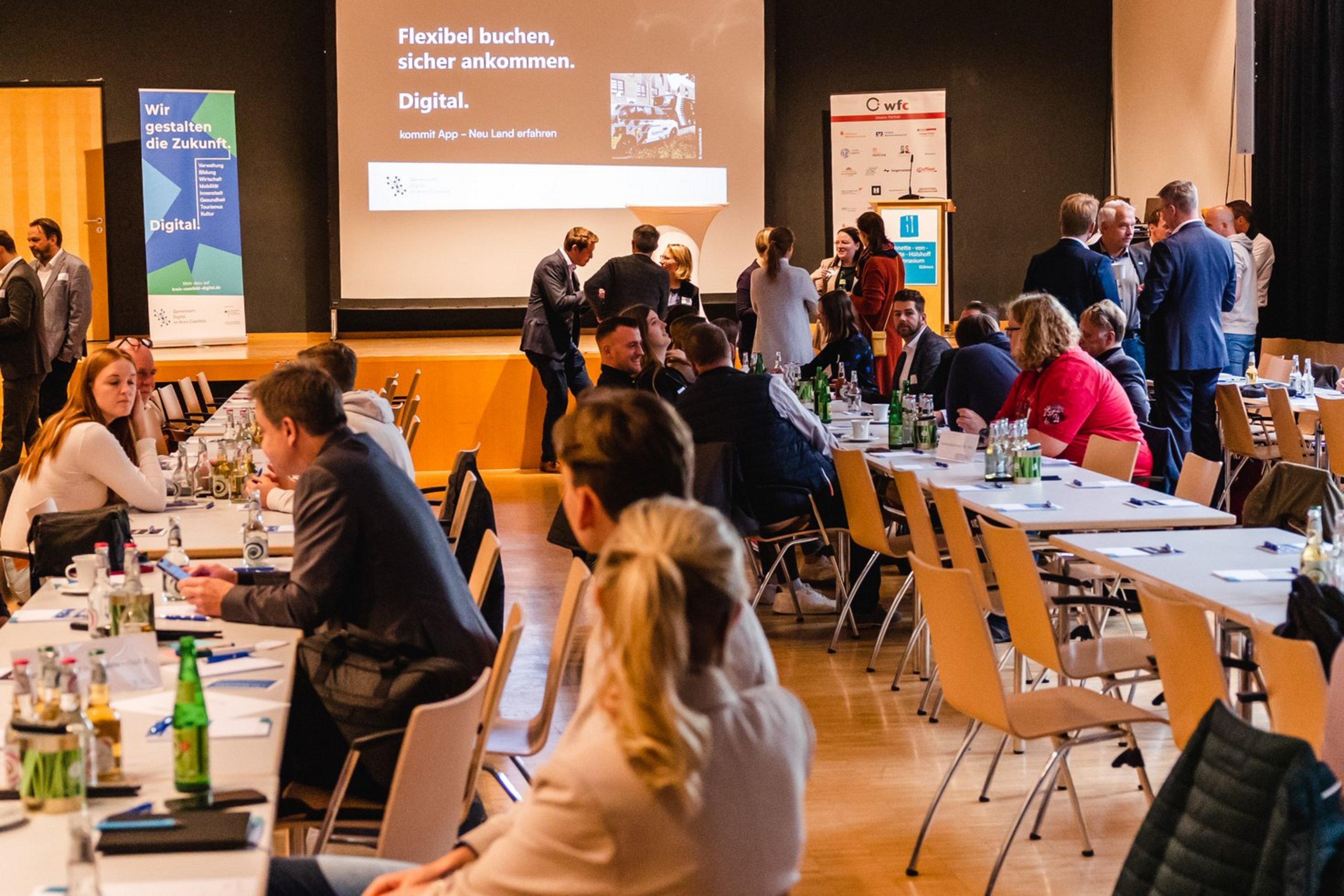 Menschen sitzen an langen Tischen in einem Konferenzraum und unterhalten sich