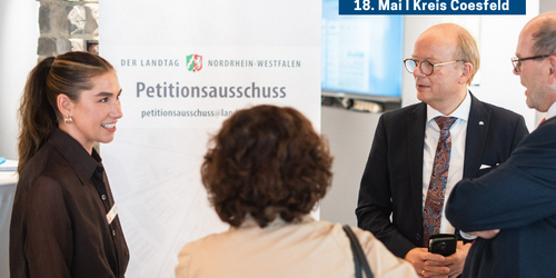 Mehrere Personen stehen im Gespräch vor einem Roll-up des Petitionsausschusses des Landtags Nordrhein-Westfalen. Oben rechts im Bild befindet sich der Hinweis „Landtag lokal – 18. Mai | Kreis Coesfeld“.