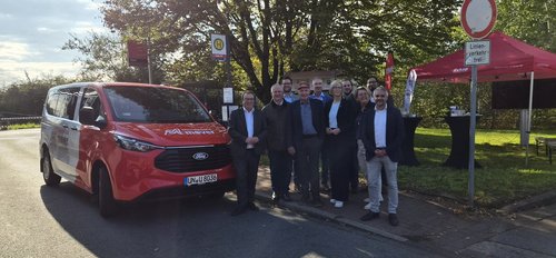 Zehn Männer und Frauen stehen neben einem roten Transporter auf dessen Motorhaube Münsterland Mover steht.