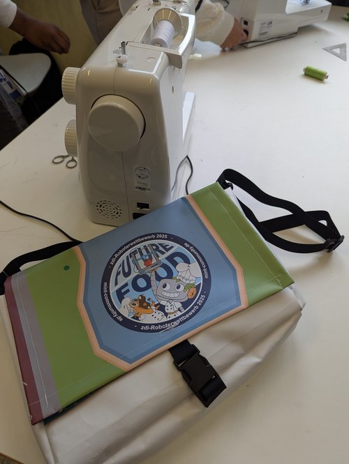 Eine selbstgenähte Umhängetasche mit „Future Food“-Motiv liegt neben einer Nähmaschine auf dem Tisch.
