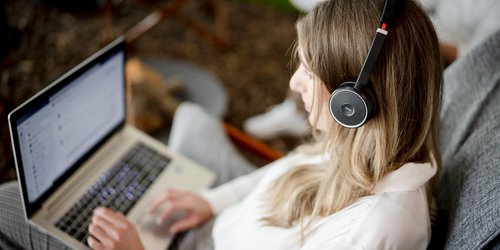 Eine junge Frau sitzt mit einem Laptop auf dem Schoß im Freien.