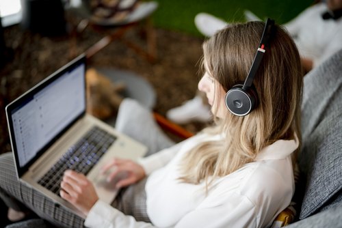 Eine junge Frau sitzt mit einem Laptop auf dem Schoß im Freien.