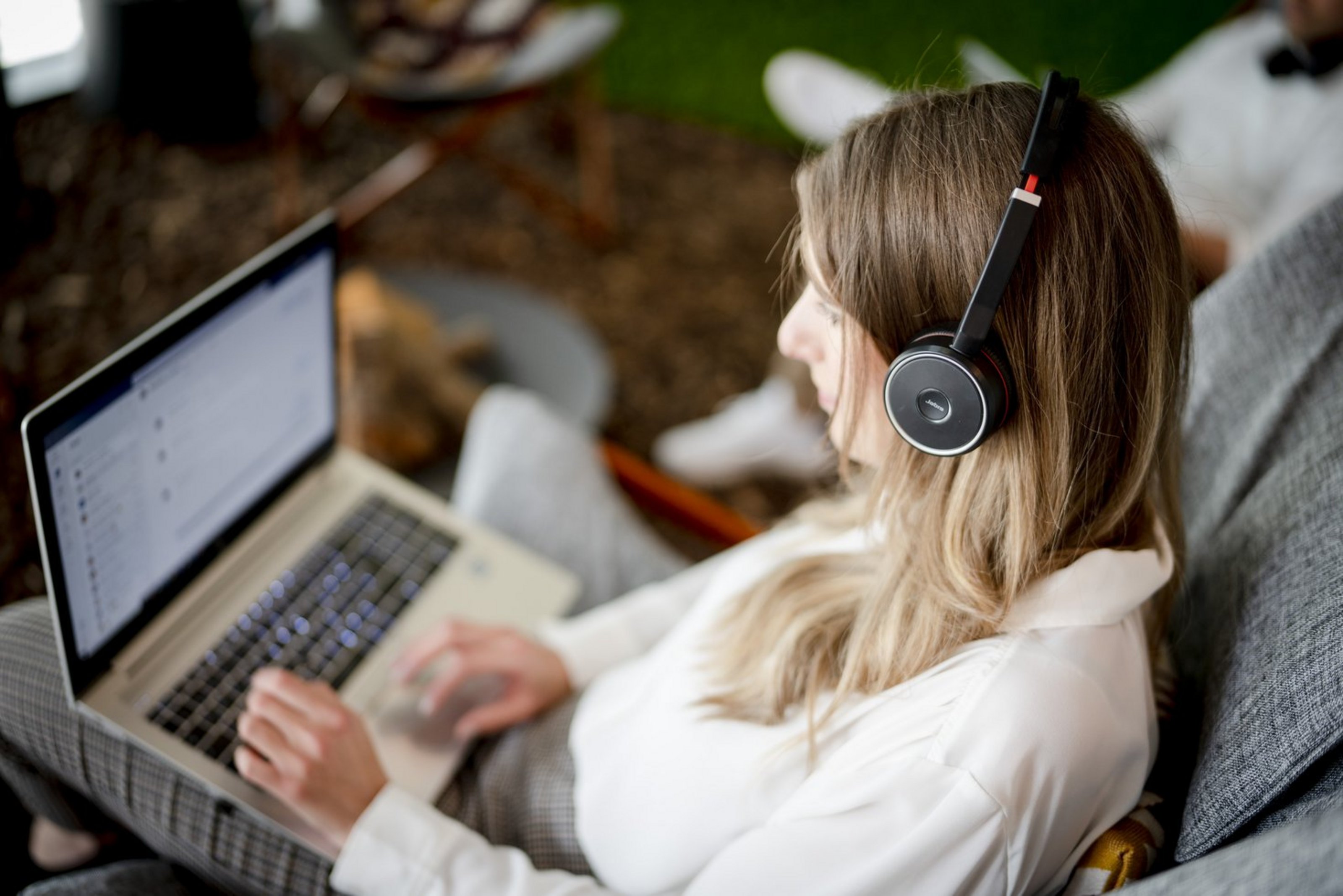 Eine junge Frau sitzt mit einem Laptop auf dem Schoß im Freien.