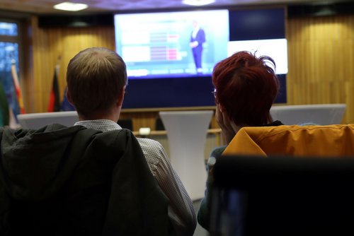 Zwei Personen verfolgen im Wahlstudio des Kreishauses die Übertragung auf einer Leinwand.
