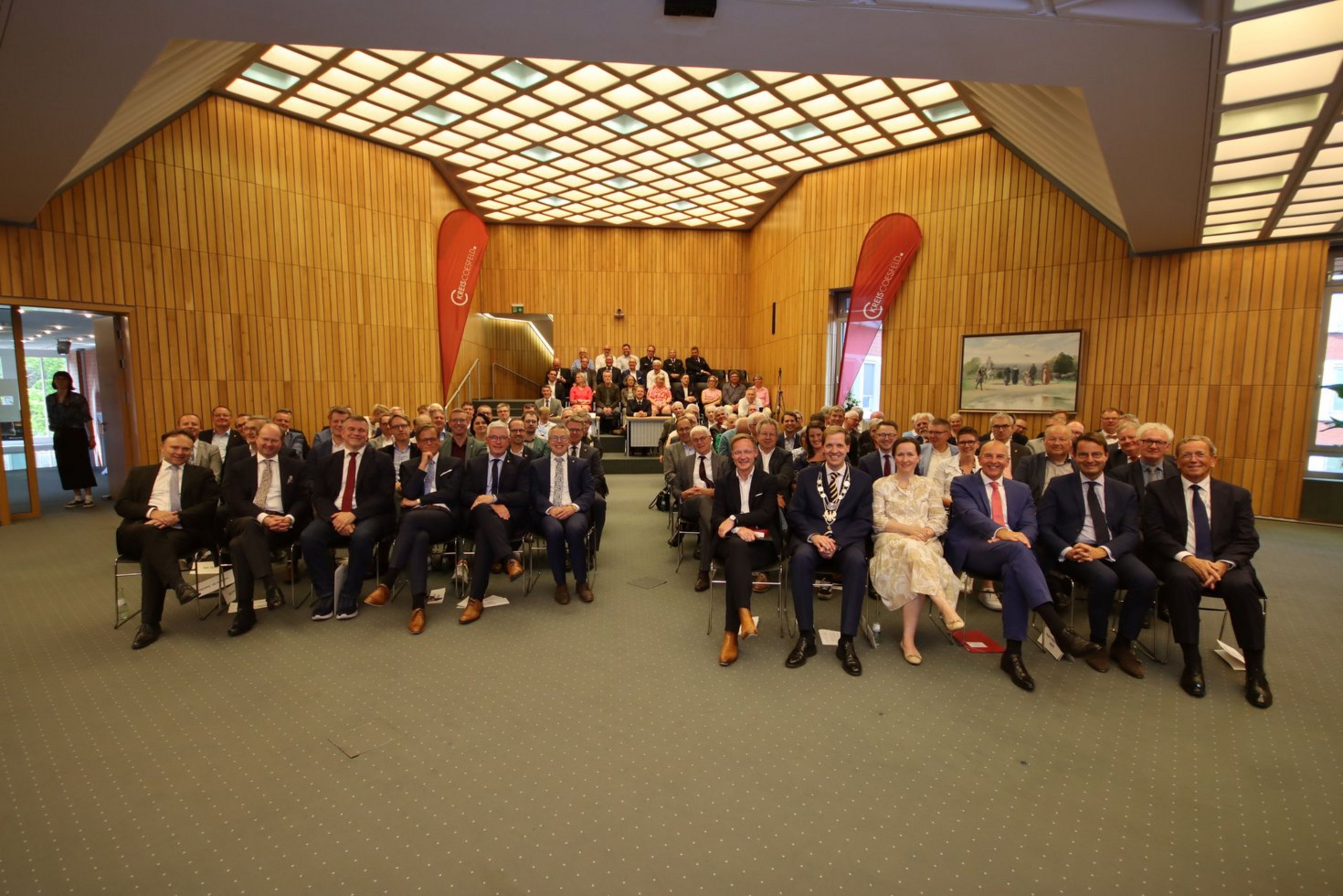 Vollbesetzter Sitzungssaal – rund 120 Gäste nahmen an der Sondersitzung des Kreistags teil (Foto: Kreis Coesfeld). In einem Sitzungssaal sitzen zahlreiche Personen in mehreren Stuhlreihen und schauen in die Kamera. Zwei rote Banner tragen die Aufschrift "Kreis Coesfeld".