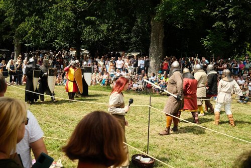 Ritter in Rüstungen und Gewändern führen vor großem Publikum eine historische Kampf-Inszenierung auf einer Wiese vor.