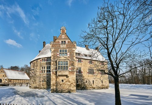 Eine eingeschneite Burg bei blauem Himmel, rechts steht ein kahler Baum.