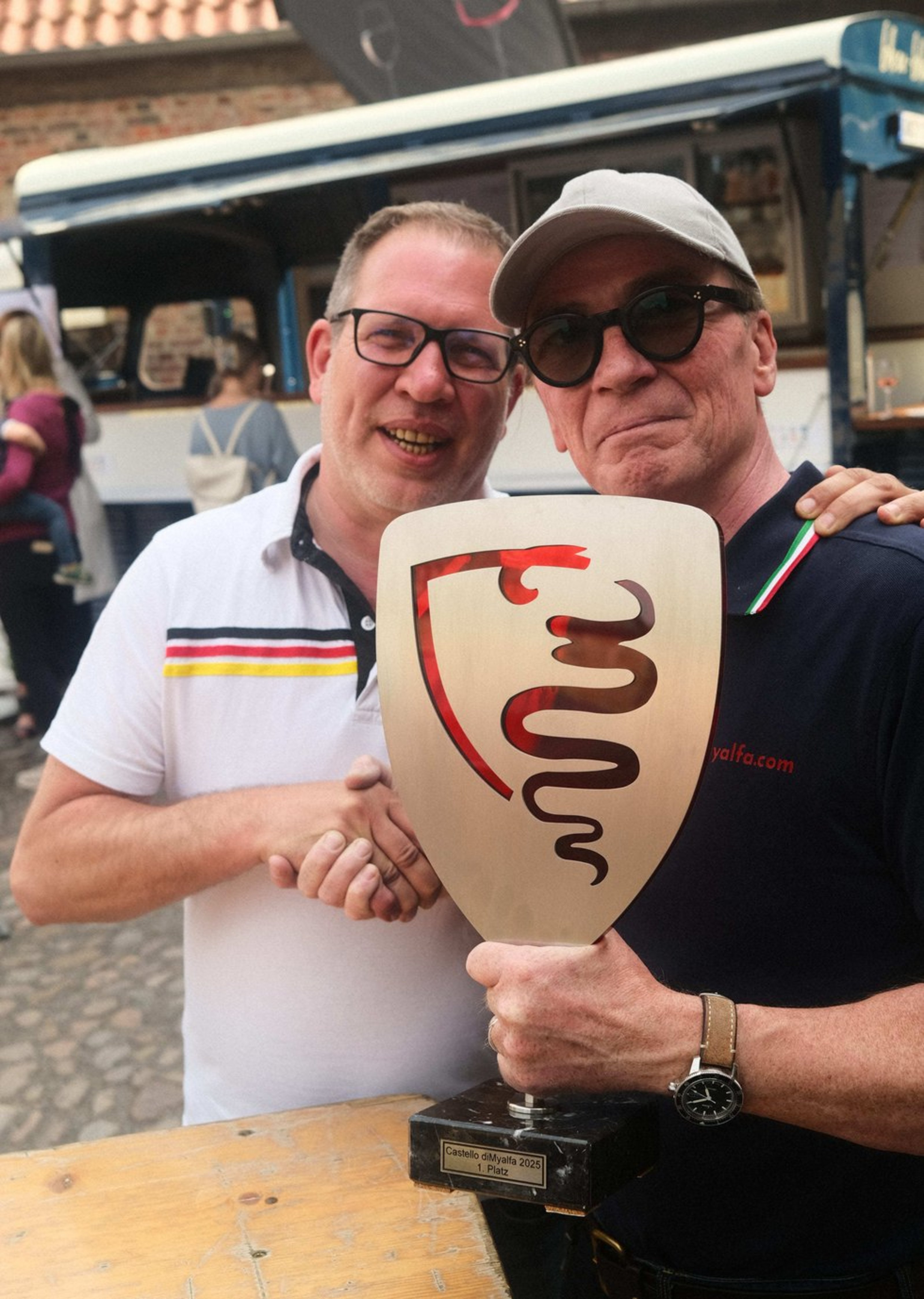 Johann Grill machte sich aus dem 700 km entfernten Starnberg auf den Weg zum Schlösser- und Burgentag zur Burg Vischering (Foto: Kreis Coesfeld). Zwei Männer schütteln sich die Hände. Einer hält einen Pokal in der Hand.