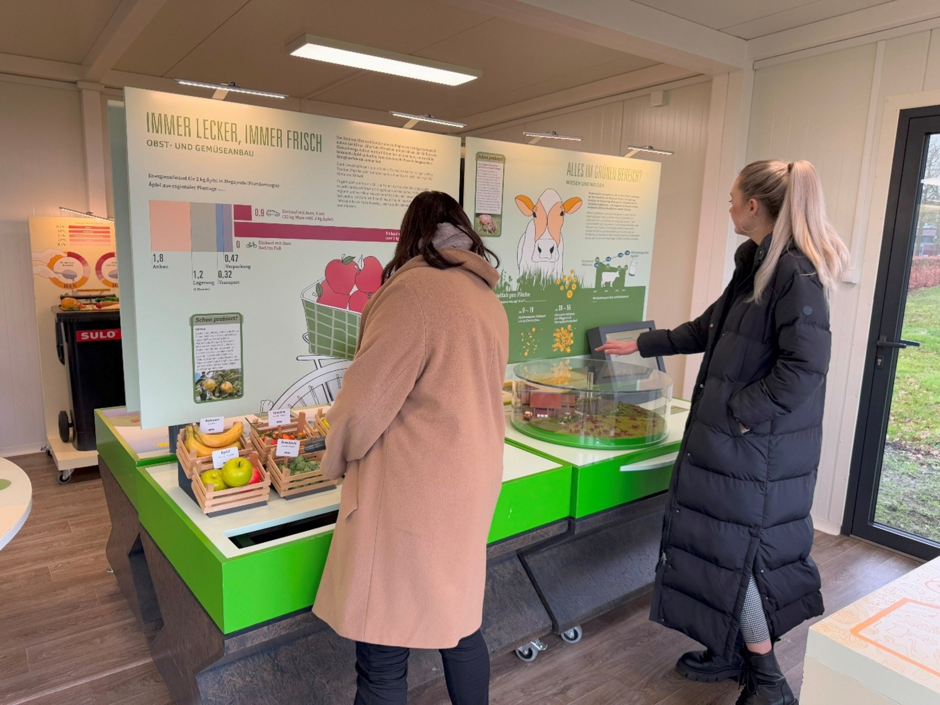 Zwei Personen stehen vor einer Schautafel mit der Aufschrift "Immer  lecker, immer frisch".