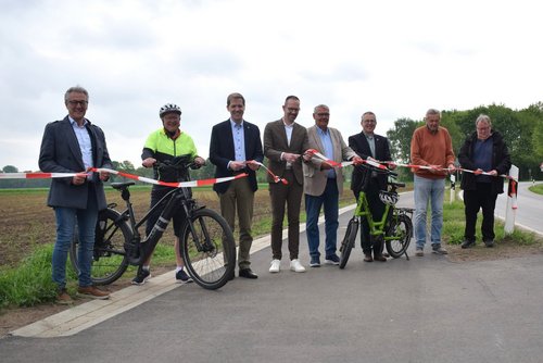 Acht Männer stehen nebeneinander auf einem Radweg und halten ein Absperrband in den Händen, das von den Personen zerschnitten wird.
