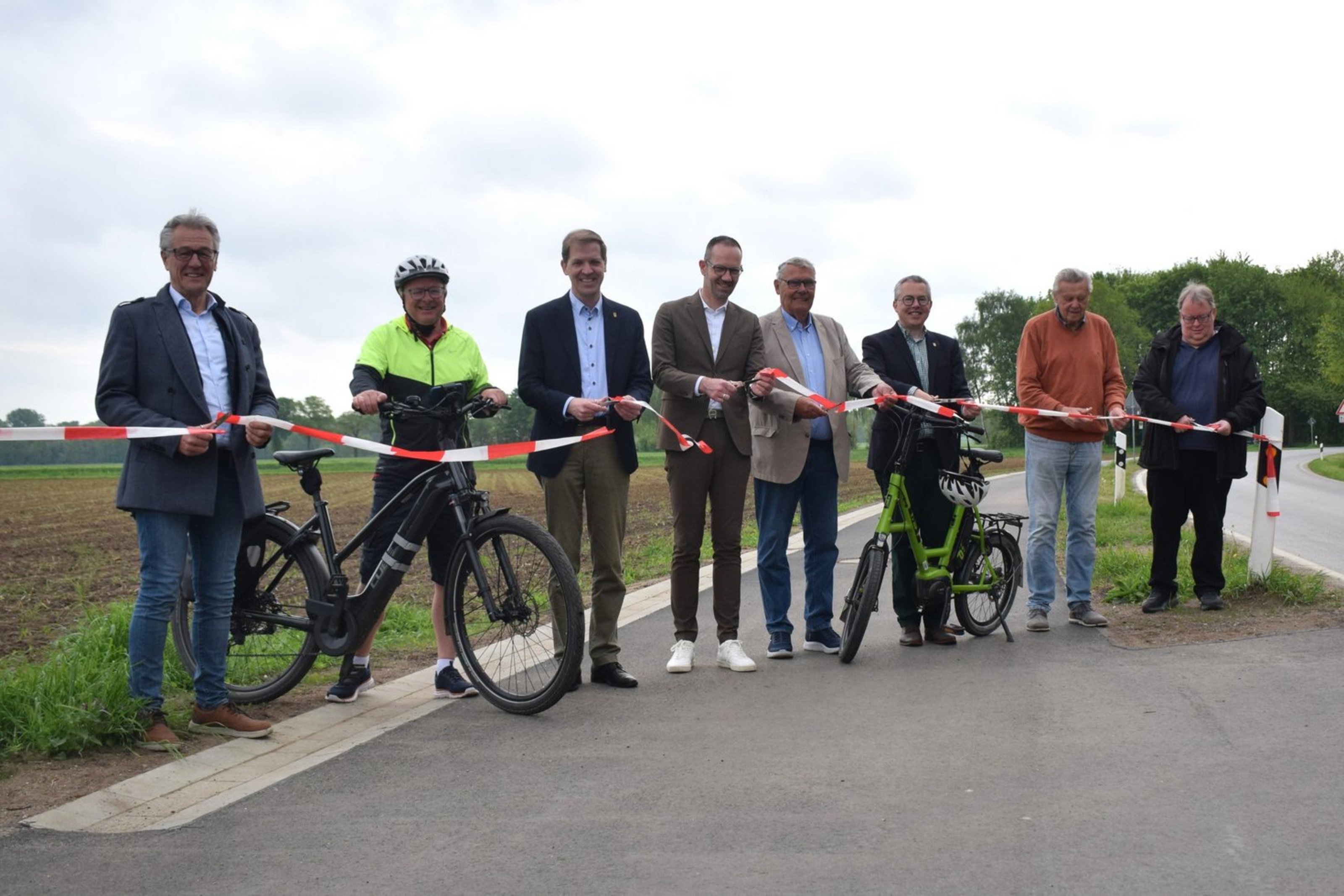 Acht Männer stehen nebeneinander auf einem Radweg und halten ein Absperrband in den Händen, das von den Personen zerschnitten wird.
