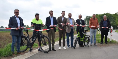 Acht Männer stehen nebeneinander auf einem Radweg und halten ein Absperrband in den Händen, das von den Personen zerschnitten wird.