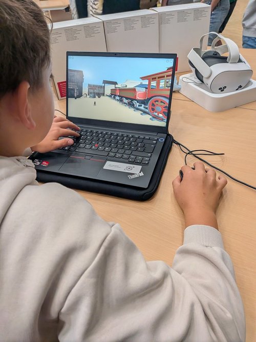 Ein Schüler arbeitet an einem Computer. Auf dem Bildschirm ist eine virtuelle Darstellung einer fiktiven Welt zu sehen. 