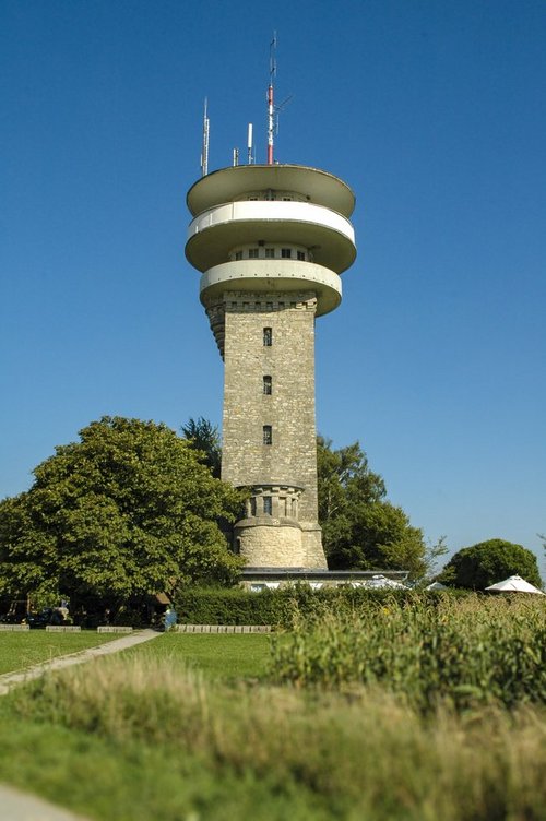Longinusturm auf einem Hügel, umgeben von Wiesen und Bäumen.
