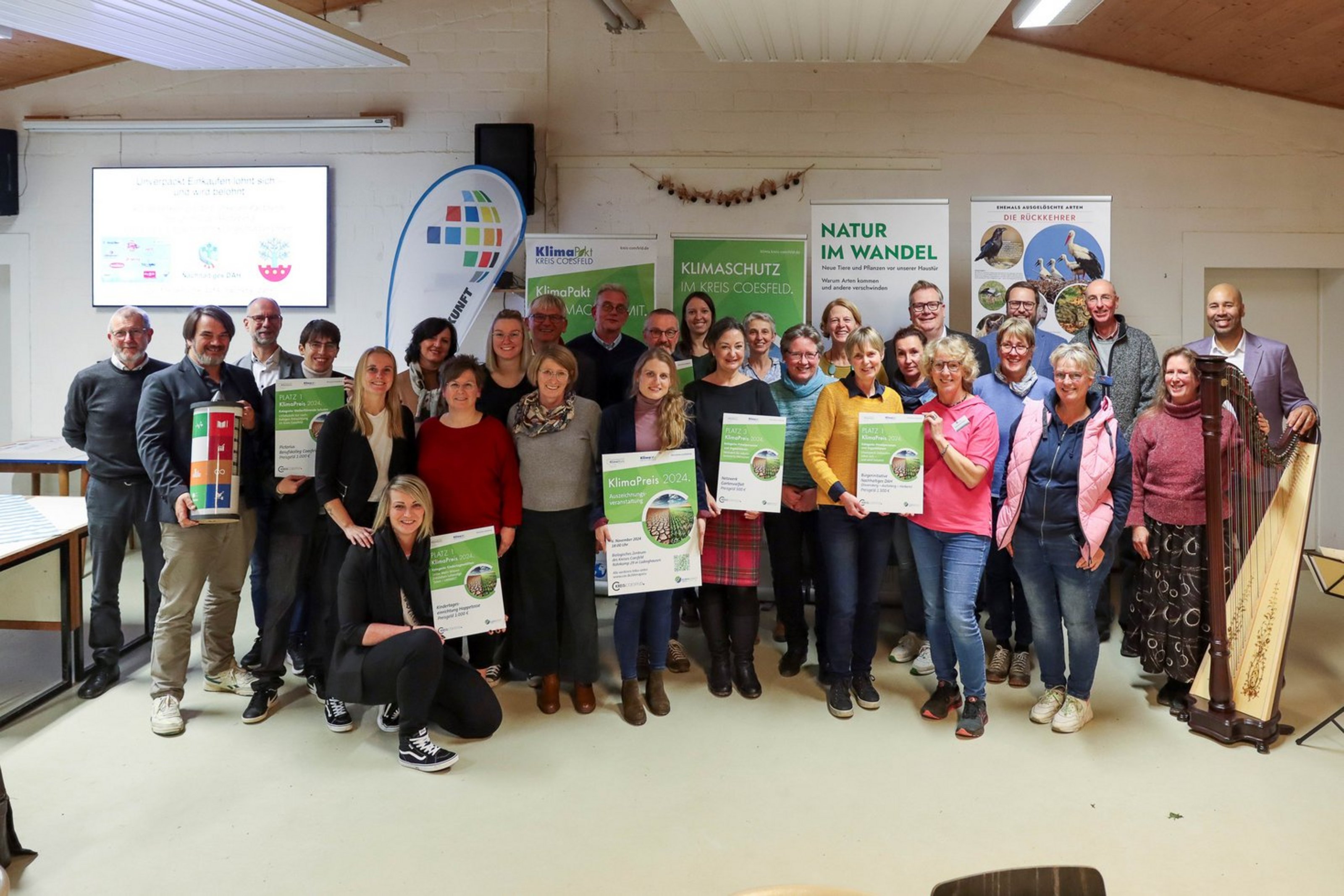 Eine große Gruppe Frauen und Männer steht zusammen in einem Raum. Einige Personen halten eine große weiß grüne Urkunde in der Hand.