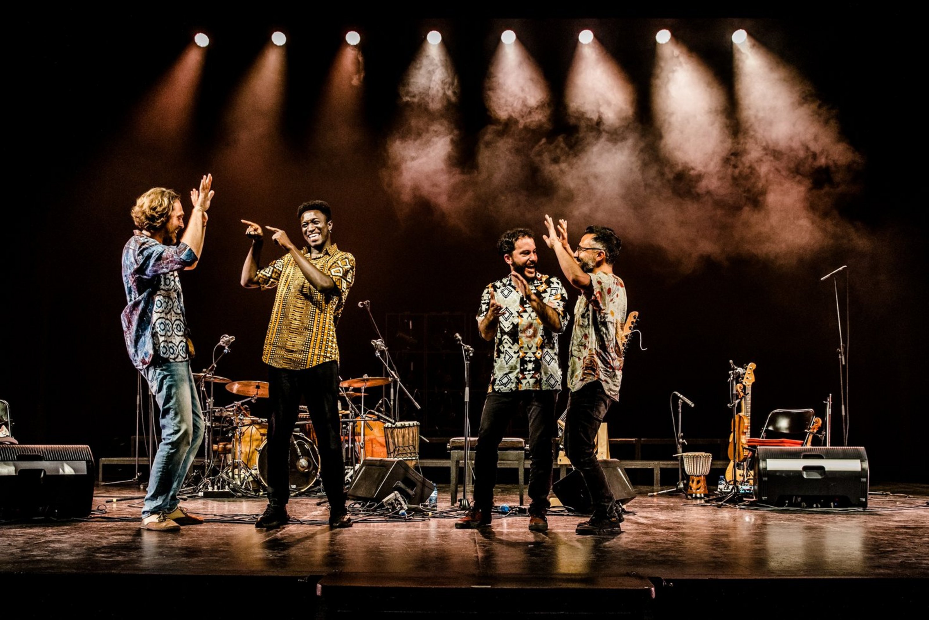 Das Finale des Münsterland Festivals findet auf der Burg Vischering in Lüdinghausen statt. Momi Maiga bringt dabei die Klangtraditionen Westafrikas mit der Leichtigkeit Spaniens zusammen (Foto: Andreu Doz). Auf einer Bühne stehen vier Männer in bunten Hemden. Im Hintergrund sind ein Schlagzeug, eine Gitarre, eine Trommel und Lautsprecher zu sehen.
