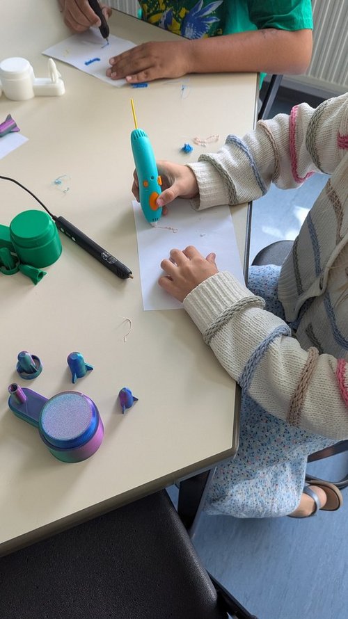 Man sieht die Hände eines Kindes, das einen großen Stift hält. Aus dem Stift kommt ein festes Material, das strichförmig auf einem Blatt Papier liegt.