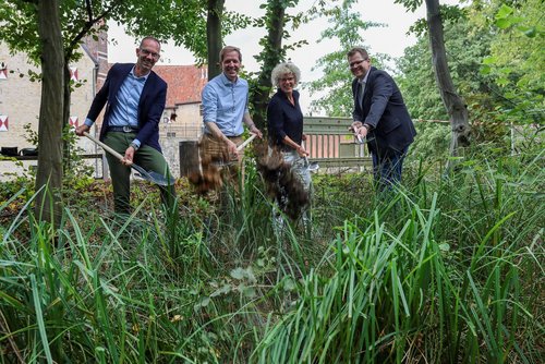Vier Personen stehen am Rand der Außengräfte und halten für den symbolischen Spatenstich die Grabwerkzeuge in der Hand. 