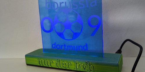 Eine gravierte LED-Acryl-Lampe steht auf einem gelben Sockel, auf dem "nur der bvb" steht. Auf der darauf stehenden blauen Platte steht "borussia 09 dortmund". 