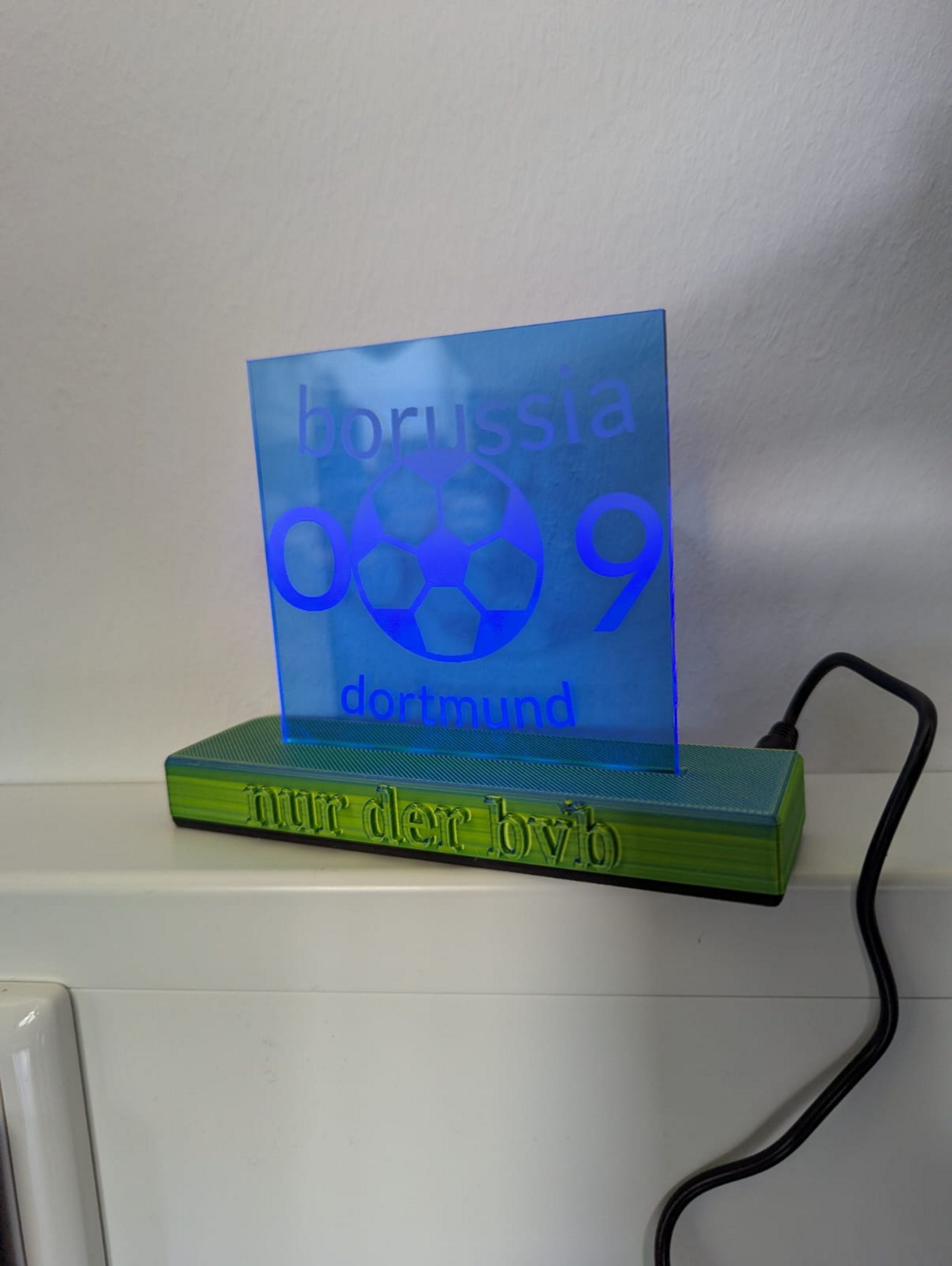 Eine gravierte LED-Acryl-Lampe steht auf einem gelben Sockel, auf dem "nur der bvb" steht. Auf der darauf stehenden blauen Platte steht "borussia 09 dortmund". 