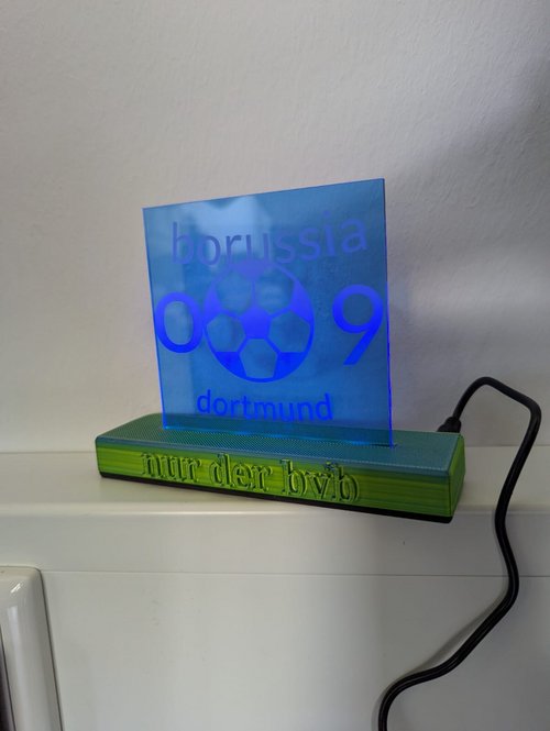 Eine gravierte LED-Acryl-Lampe steht auf einem gelben Sockel, auf dem "nur der bvb" steht. Auf der darauf stehenden blauen Platte steht "borussia 09 dortmund". 