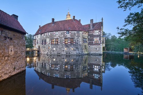 Beleuchtete Burg Vischering spiegelt sich abends im Wassergraben.