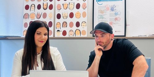 Eine Frau und ein Mann sitzen zusammen an einem Tisch und schauen auf einen Laptop Bildschirm.
