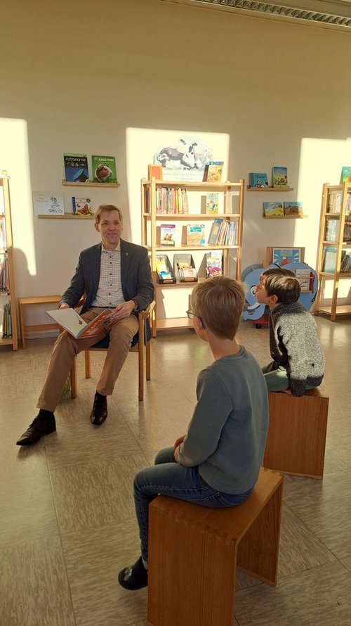 Landrat Dr. Schulze Pellengahr liest in einem Klassenzimmer mehreren Kindern aus einem Kinderbuch vor. 