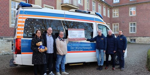 Sechs Personen stehen vor einem Kastenwagen mit der Aufschrift "Der Wünschewagen - Letzte Wünsche wagen". Zwei Personen halten eine Scheck-Tafel. 
