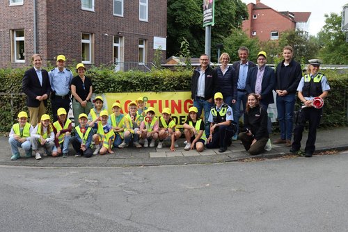 Kinder mit gelben Mützen knien vor einem Banner zur Verkehrssicherheitsaktion "Kreis Coesfeld sieht gelb!". Rechts und links der Gruppe stehen Erwachsene. 